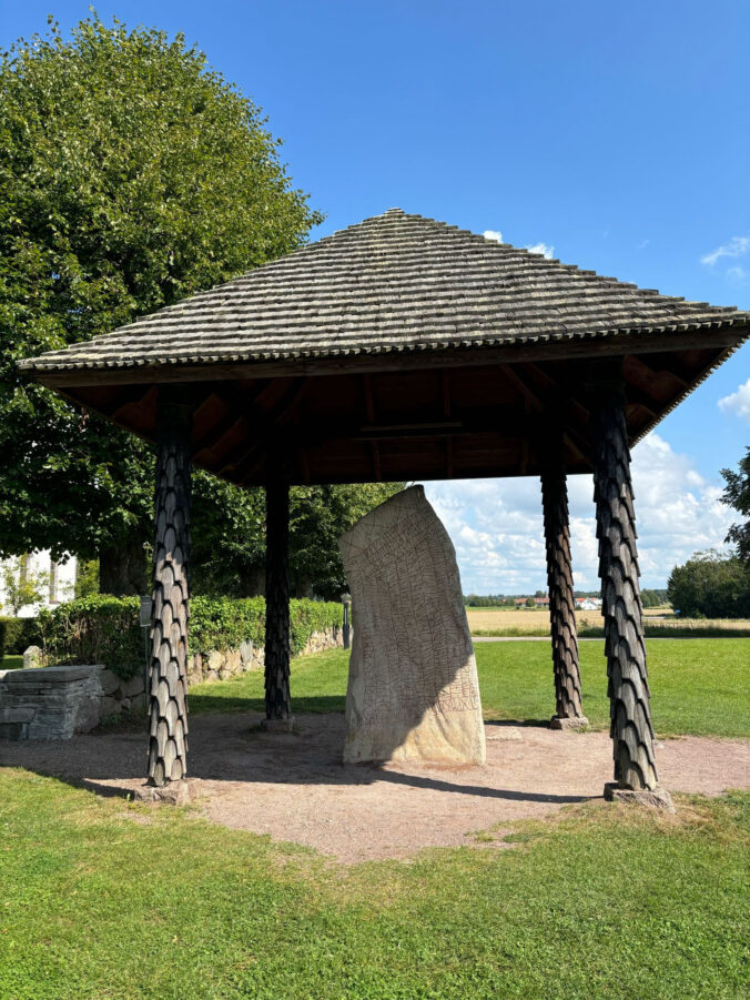 Runenstein unter Dachkonstruktion.